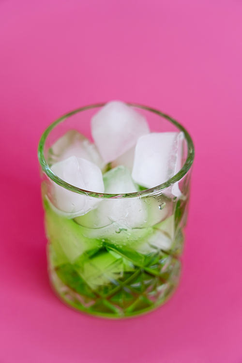close up of frozen ice cubes in glass with green mojito drink on pink
