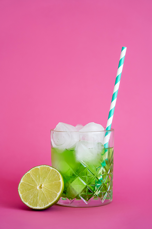 frozen ice cubes in glass with green mojito drink near sliced lime on pink