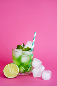 frozen ice cubes in glass with green mojito with straw and mint near lime on pink