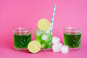 frozen ice cubes in glass with mojito near green beverages and limes on pink
