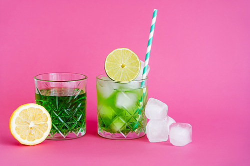 ice cubes in glass with mojito near green beverage and limes on pink