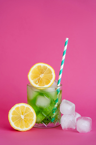 ice cubes in glass with mojito drink and straw near lemons on pink