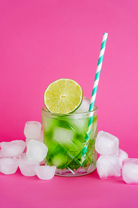 ice cubes in faceted glass with mojito drink and sliced lime on pink