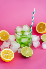 frozen ice cubes in glass with mojito drink and straw near citrus fruits on pink