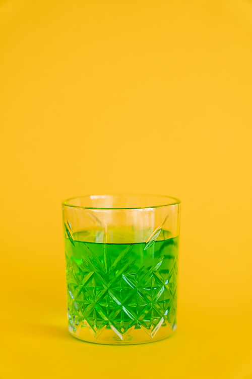 faceted glass with green alcohol drink on yellow