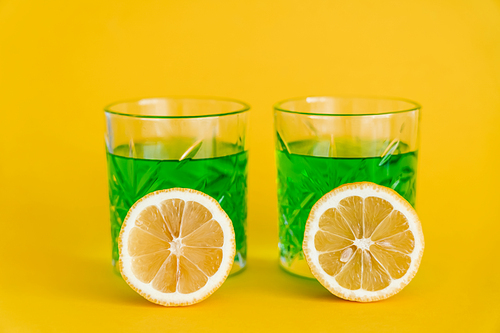 faceted glasses with green alcohol drink and sliced lemons on yellow