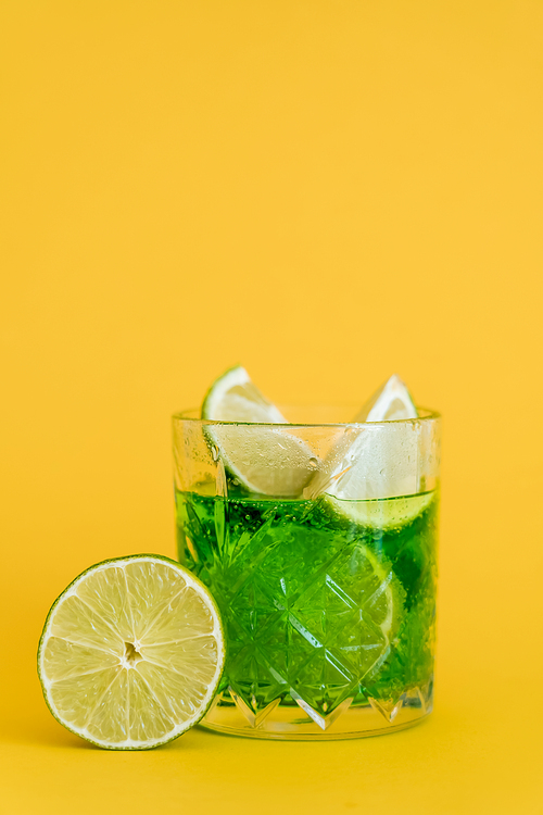 sliced limes in glass with sparkling mojito drink on yellow