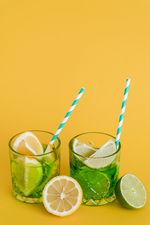 sliced citrus fruits in glasses with sparkling mojito drink and straws on yellow
