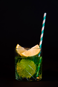sliced citrus fruits in glass with alcohol drink and straw isolated on black
