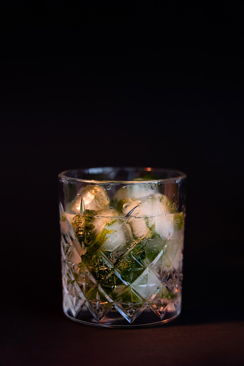 cool faceted glass with rum and ice cubes isolated on black