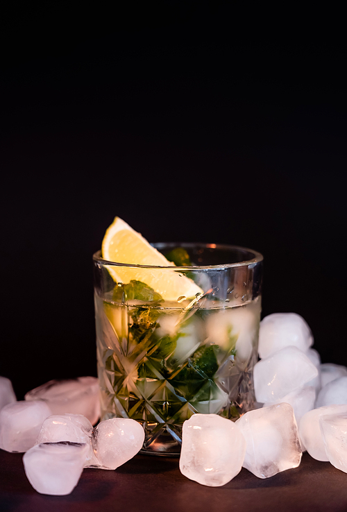 cool faceted glass with mojito near ice cubes on black