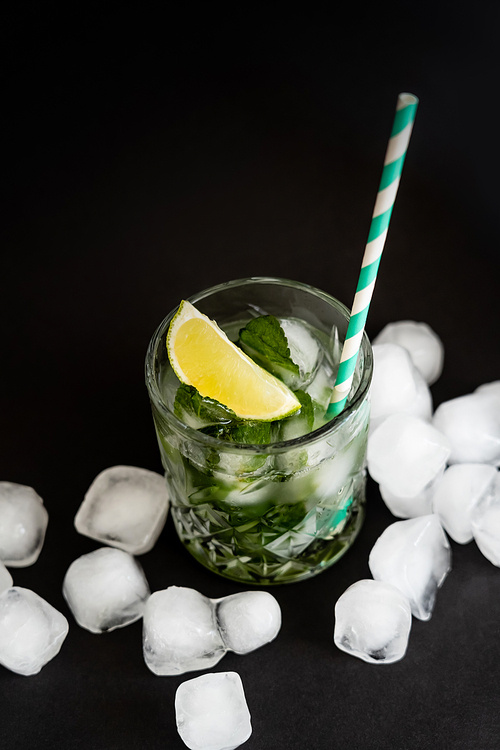 high angle view of cool faceted glass with mojito near ice cubes on black