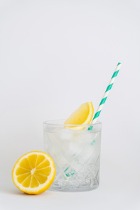 faceted cold glass with ice cubes, paper straw and sliced lemons on white