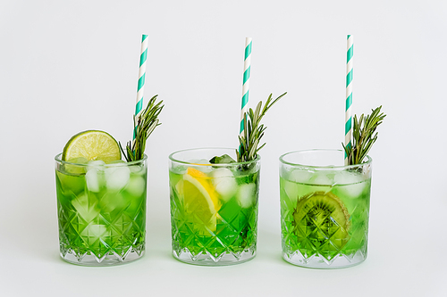 faceted glasses with green cocktail, ice cubes and fruits on white