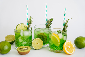 faceted glasses with cold green cocktail, straws and fruits on white