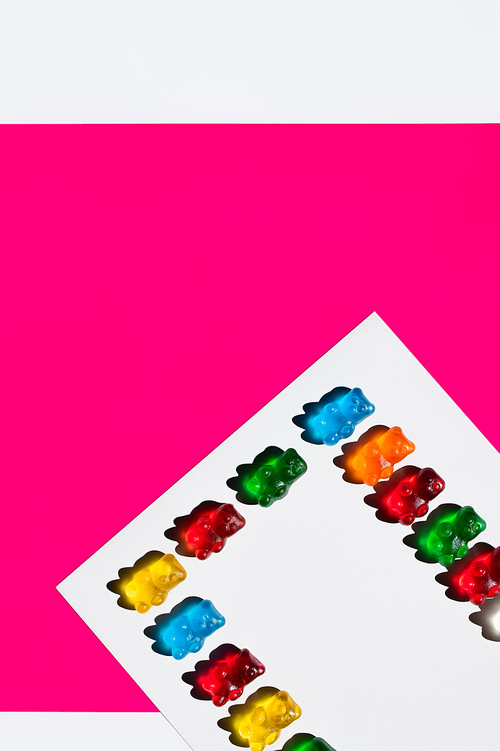 Flat lay of colorful gummy bears on white and pink background