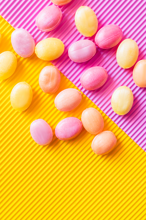 Top view of colorful sweets on textured pink and yellow background