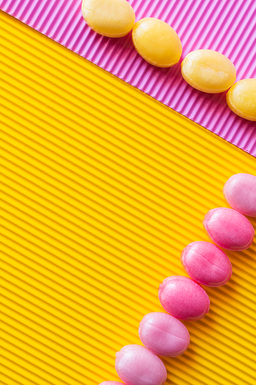 Flat lay of colorful sweets on textured pink and yellow background