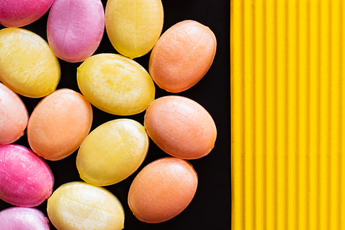 Top view of sweet candies on black and textured yellow surface