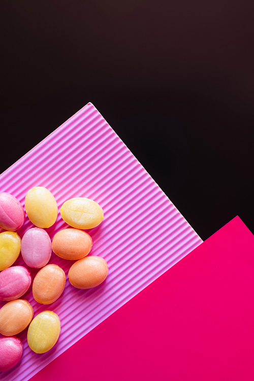 Top view of colorful candies on pink surface isolated on black