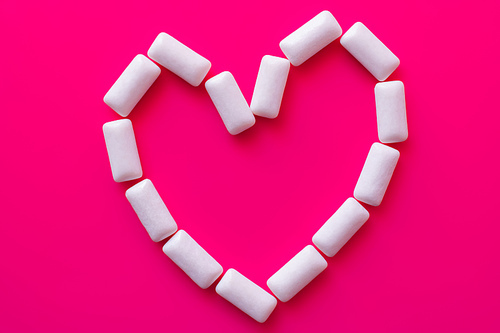 Top view of heart shape from white chewing gums on pink background