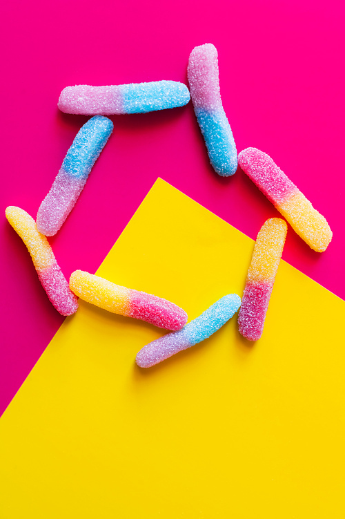 Flat lay with delicious jelly sweets on pink and yellow background