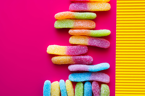 Flat lay of colorful jelly sweets on pink and textured yellow surface