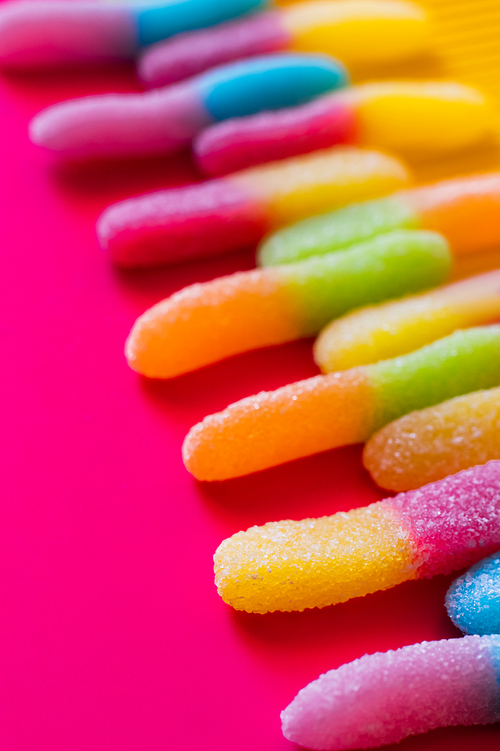 Close up view of jelly sweets in sugar on pink and yellow surface