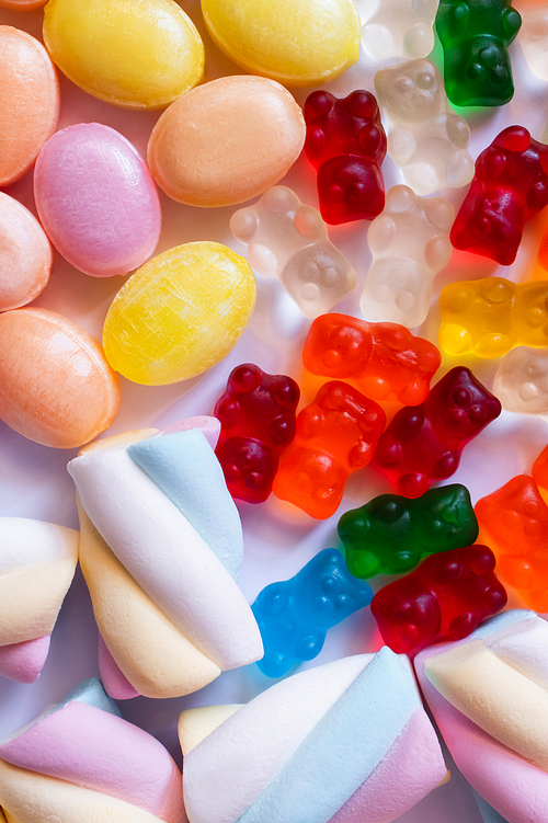 Close up view of marshmallows and colorful sweets on white background