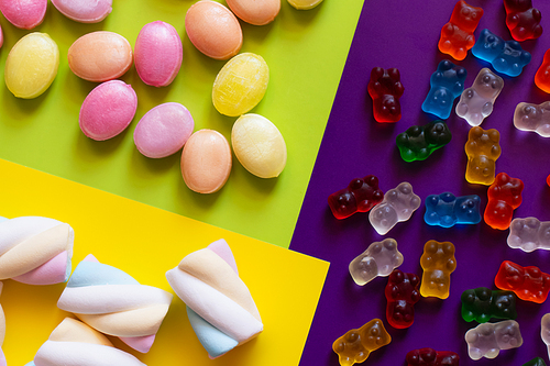 Flat lay of marshmallows near candies and jelly bears on colorful surface