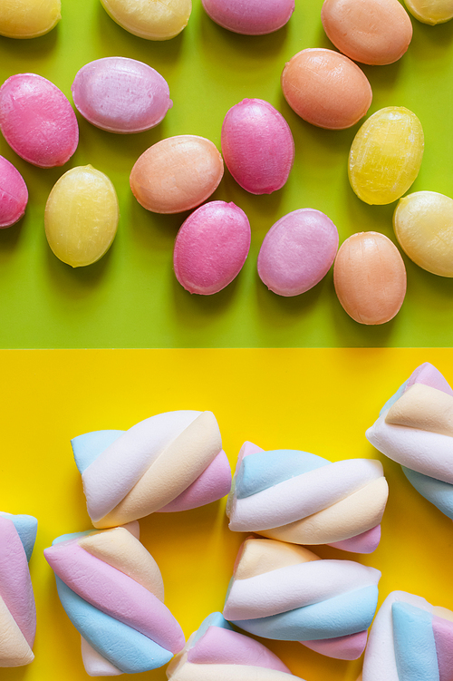 Top view of candies and marshmallows on green and yellow background