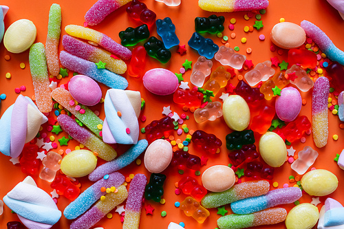 Top view of colorful jelly sweets and marshmallows on orange background