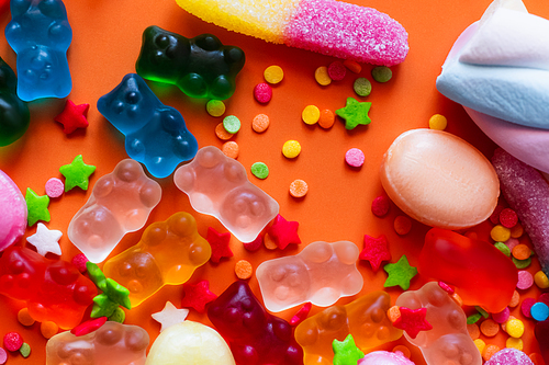 Top view of colorful jelly bears near candies and decor on orange background