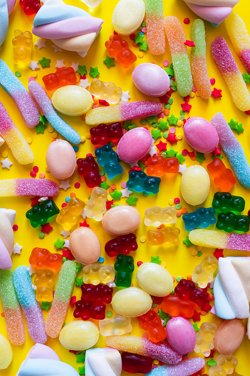Top view of colorful marshmallows and gummy bears on yellow surface