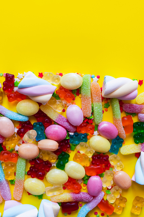 Top view of fluffy marshmallows and jelly sweets on yellow surface