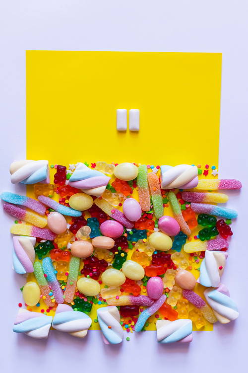 Top view of chewing gums near colorful sweets on white and yellow surface