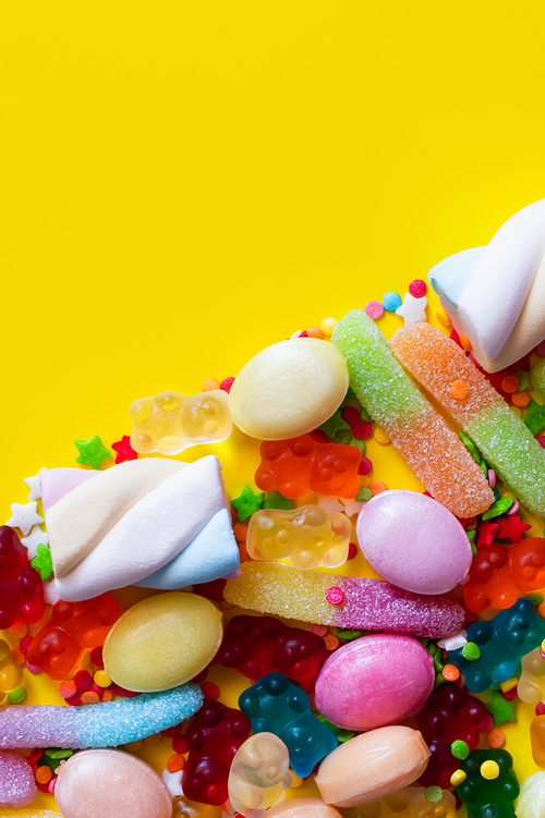Flat lay with colorful jelly sweets and tasty marshmallows on yellow background