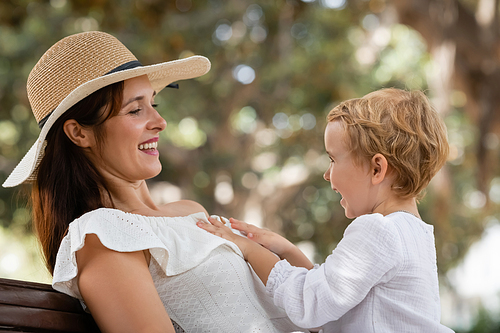 Toddler girl touching smiling mom in sun hat in park