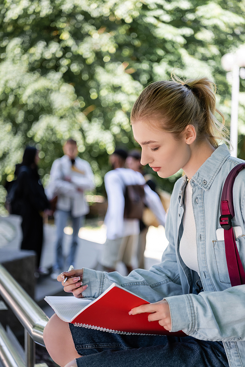 Side view of student holding pen and copy book in park