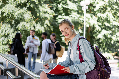 Positive student looking at camera while holding notebook in park
