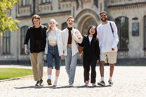 Young multiethnic students walking and looking at camera near university outdoors