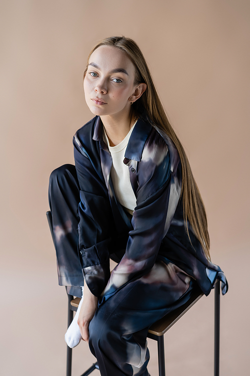 young long haired woman in tie-dye style clothes posing on chair isolated on beige