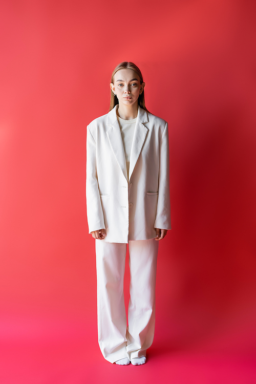 full length of woman in white suit and socks on crimson background