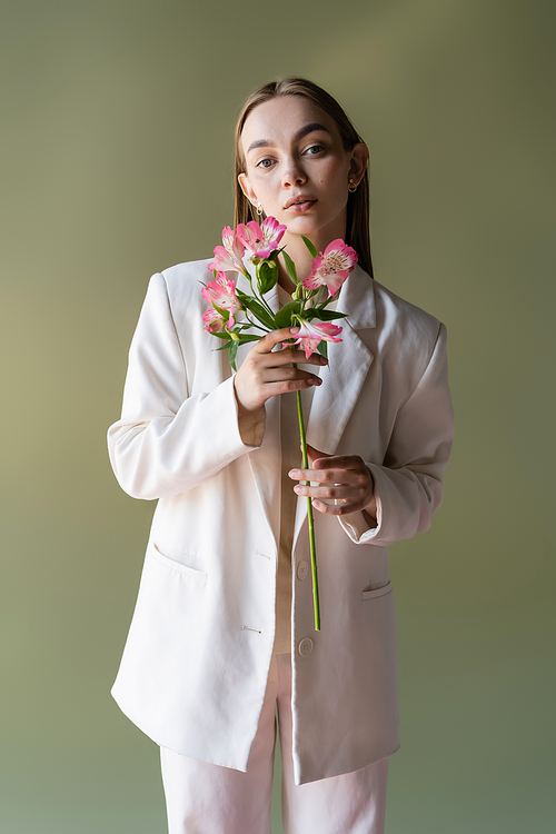 young woman in white blazer holding pink alstroemeria flowers isolated on green