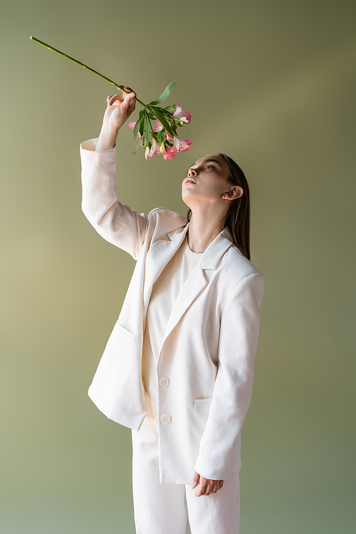 woman in white clothes holding branch of alstroemeria in raised hand isolated on green