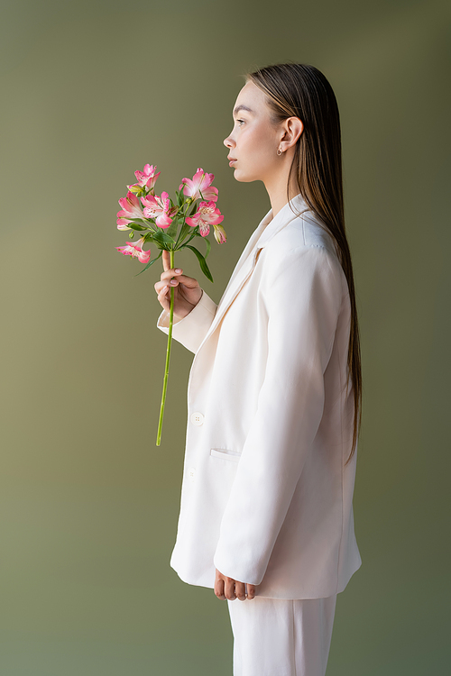 side view of woman in white blazer posing with branch of alstroemeria isolated on green