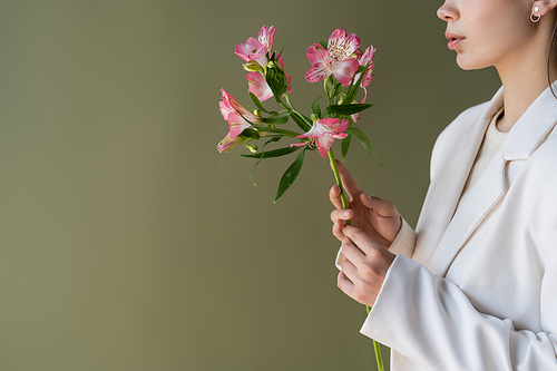 cropped view of woman in white blazer holding alstroemeria flowers isolated on green