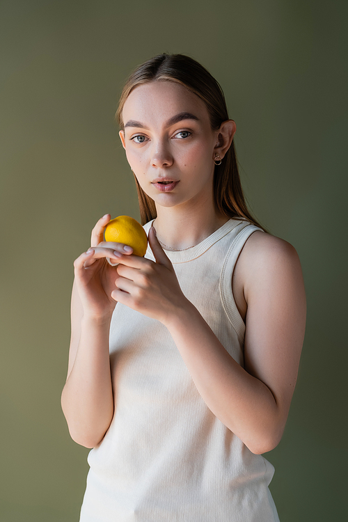 young woman with ripe lemon looking at camera isolated on green