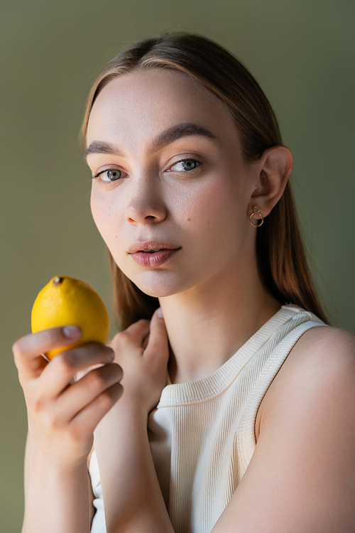 portrait of charming woman with ripe lemon looking at camera isolated on green
