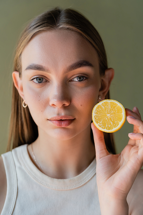 portrait of pretty young woman showing half of juicy lemon isolated on green
